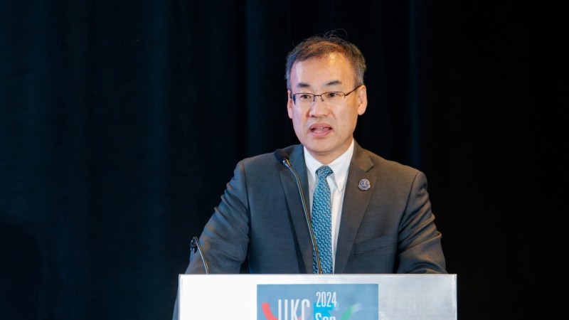 Tom Oh in suit and glasses stands speaking in front of lectern at KSEA Conference 2024