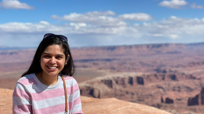 Harshala Patil wearing a pink and gray striped shirt and standing in front of mountains in the background.