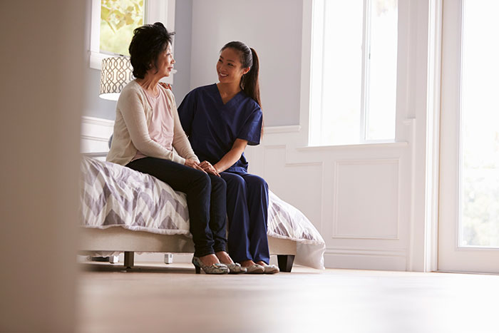 a patient and a smiling nurse sitting on a bed in a white room
