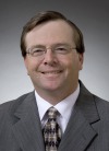 Headshot of Gerard J.  Buckley, dark brown hair, glasses, suit and stripped tie