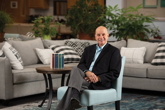 Michael Rizzolo sits in a light blue chair in a livingroom setting.