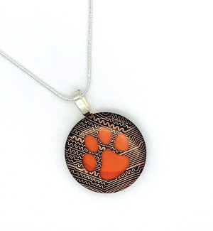 Round pendant made of circuit board with an orange paw in the center on a silver chain.