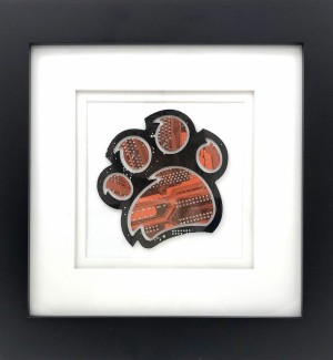 Framed orange and black Paw Print made from a cut circuit board on a white matte in a black frame.