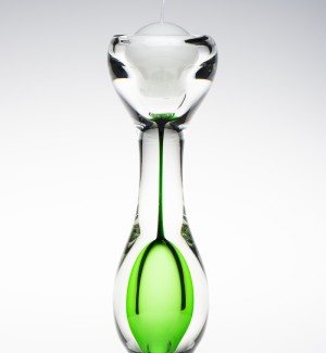 An hourglass shaped clear glass candle holder with green inside the bottom of the hourglass shape.