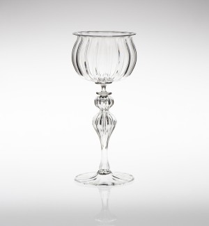 A glass goblet with intricate optical patterns standing on an hourglass shaped stem.