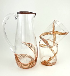 A cylindrical glass pitcher with a black rim and orange stripes sits next to two cylindrical glasses with the same orange stripe detailing.