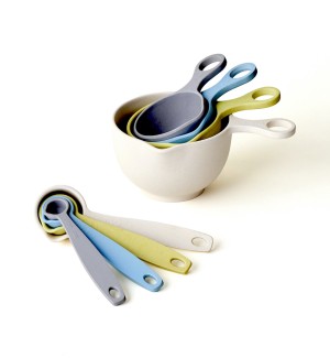 A set of 4 measuring cups in cool tone colors next to a set of measuring spoons. 