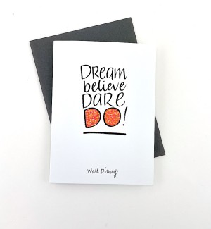 White paper greeting card with calligraphy 'Dream believe Dare DO' on cover. Dark grey envelope.