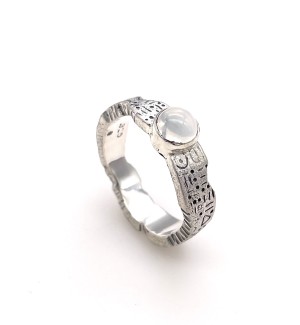 a wide band silver ring with an uneven edge and carved symbols on the surface and a moonstone setting