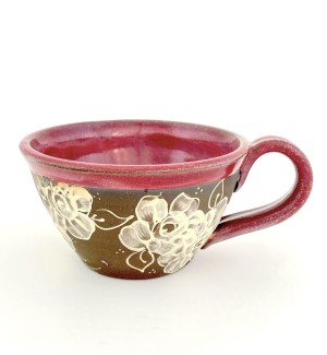 a hand thrown bowl shaped ceramic mug with a handle, a dark clay body and hand illustrated rose designs on the surface.