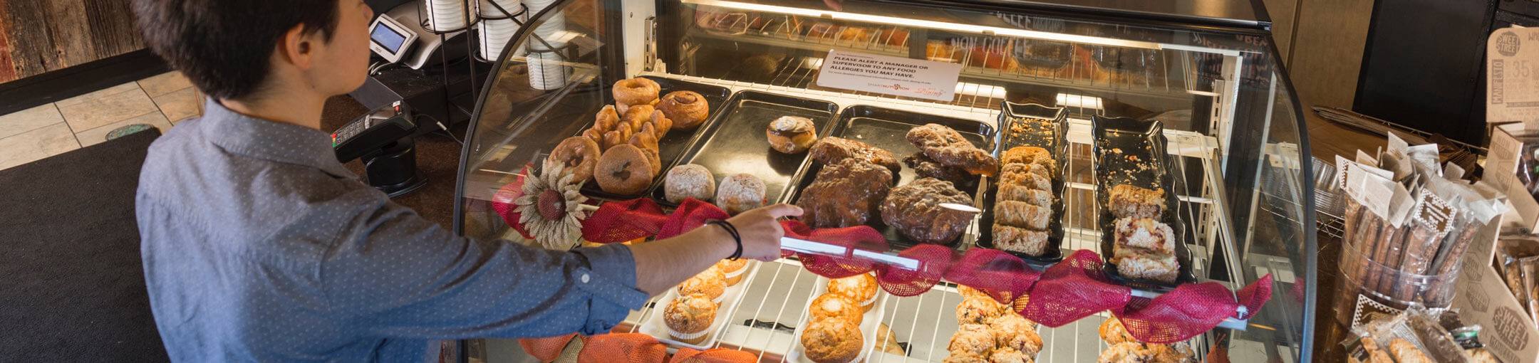A person pointing to a baked good in a display case at the Artesano Bakery and Cafe.