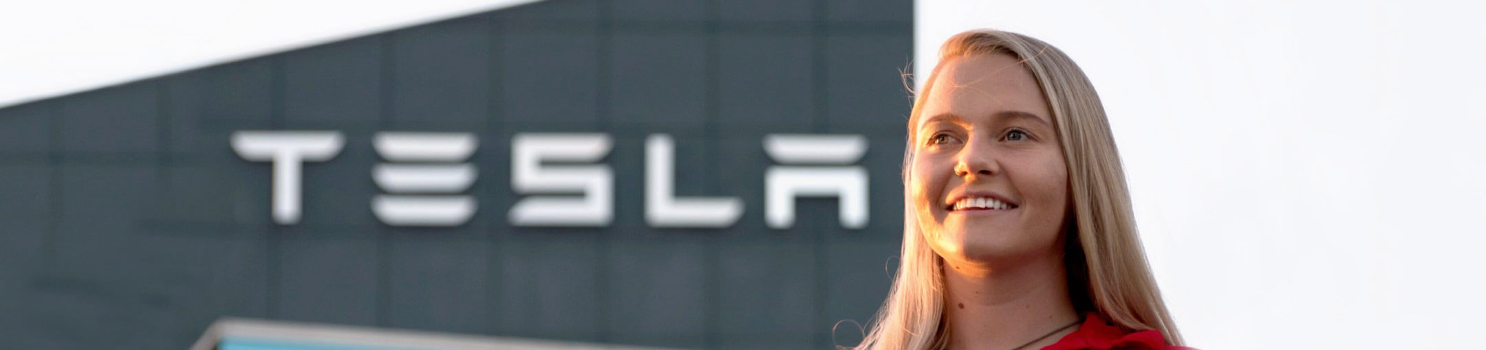 A female RIT student on co-op (cooperative education program) standing in front of a Tesla building.