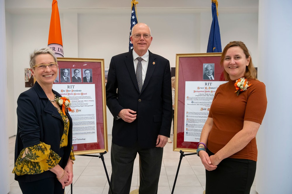 three people standing in front of two easels displaying award certificates.