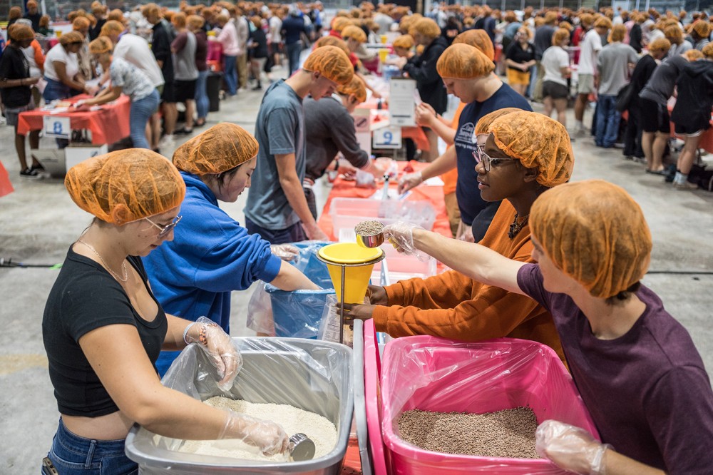 rows of college students wearing hair nets and filling bags with pasta, rice, and grains.