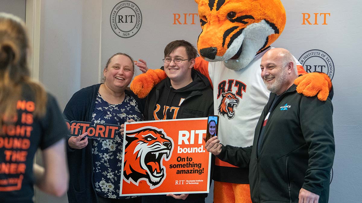 Family in R I T gear smiling with Ritchie, the tiger mascot