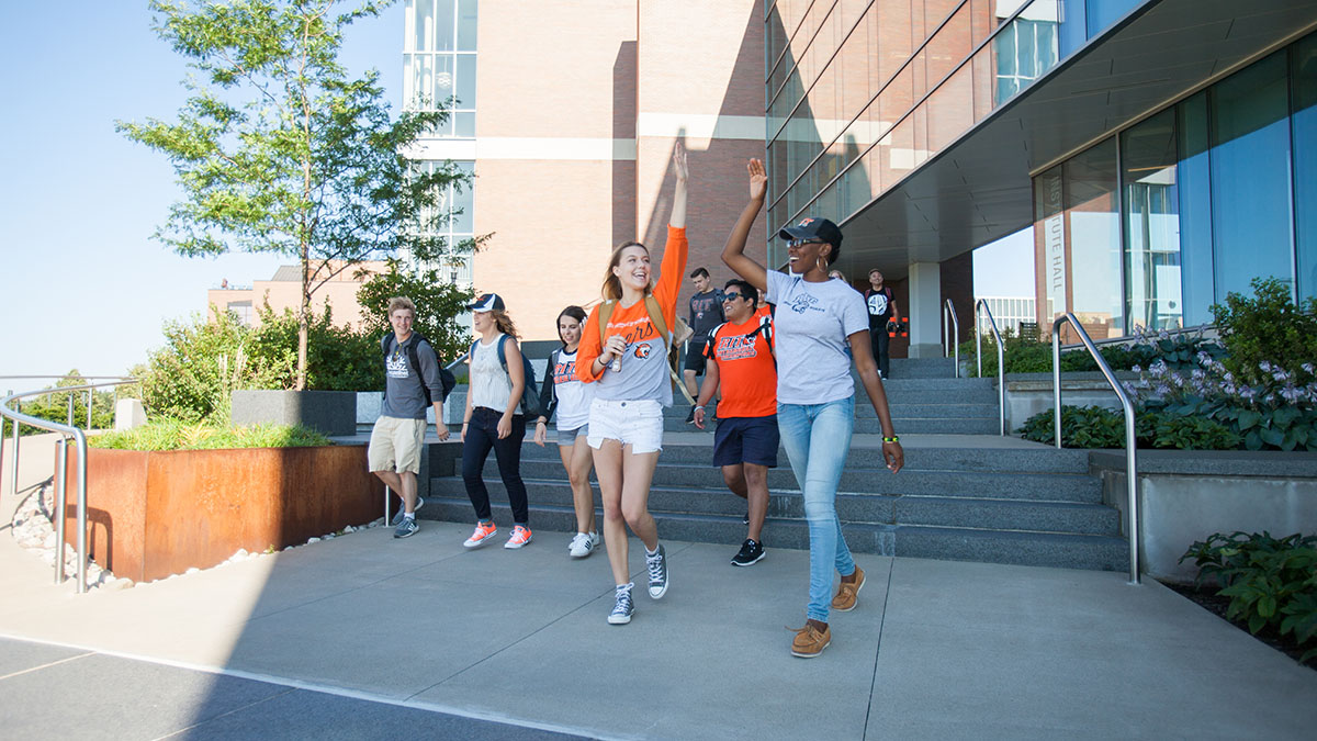 A group of students happily leaving a campus building, some raising their arms to high-five.