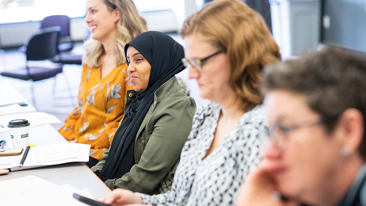 A group of people seated at a table, participating in a meeting or workshop, with one woman smiling attentively.