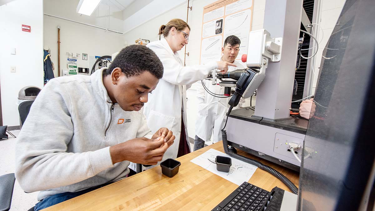 Students in a lab performing hands-on experiments, working with machines and data on a computer.