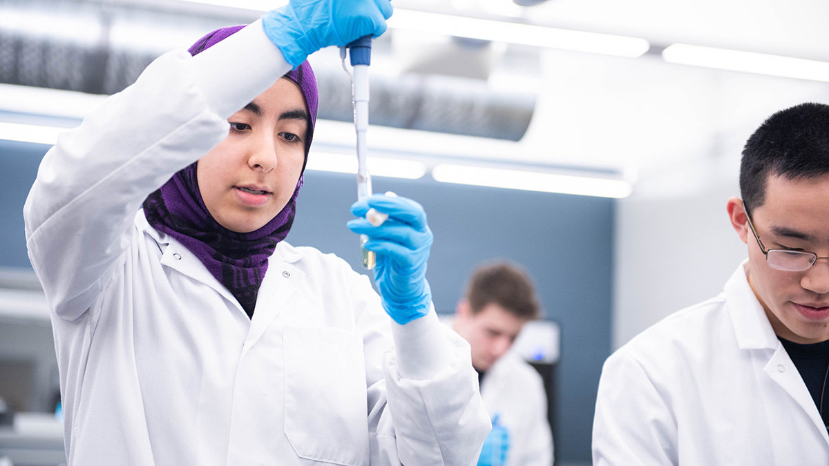 student researcher wearing a lab coat and using a pipette.