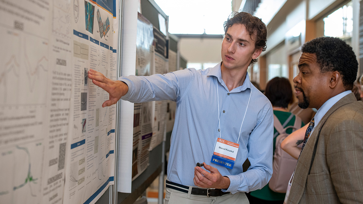 A man presenting a research poster to an audience member at an academic conference.