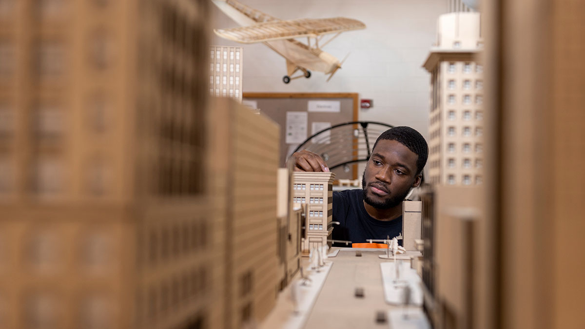 A student carefully adjusting a miniature building model as part of an architecture project.