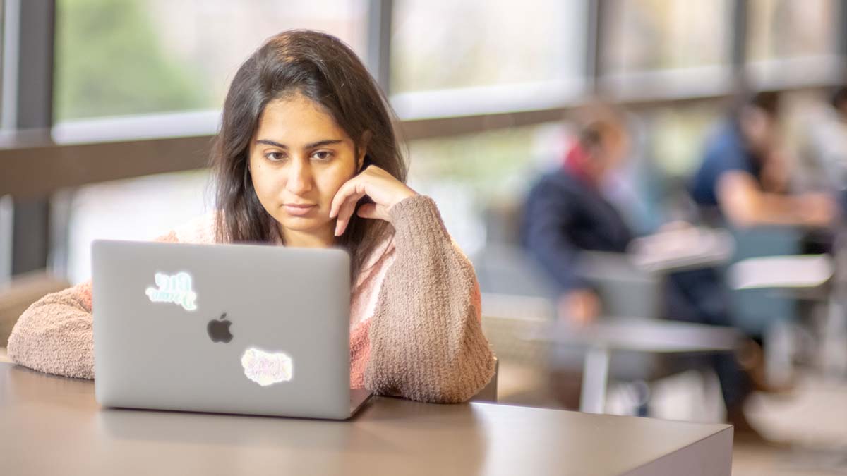 A student working on a laptop with focused expression in a study lounge.