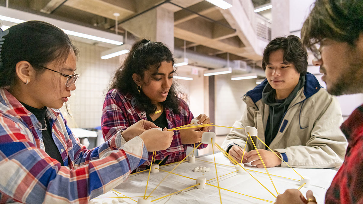 Four students collaborating to build a structure using marshmallows and uncooked spaghetti during a workshop.