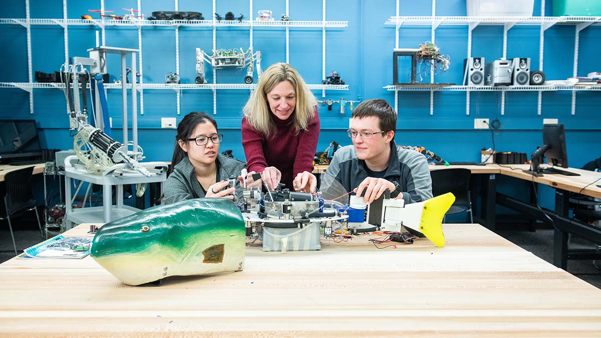 A group of students and a professor working on a robotic fish project in a lab.