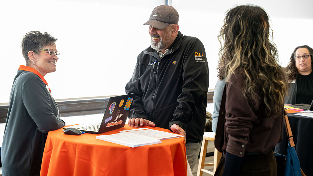 Two staff and a visitor interacting at a table with a laptop and informational material.