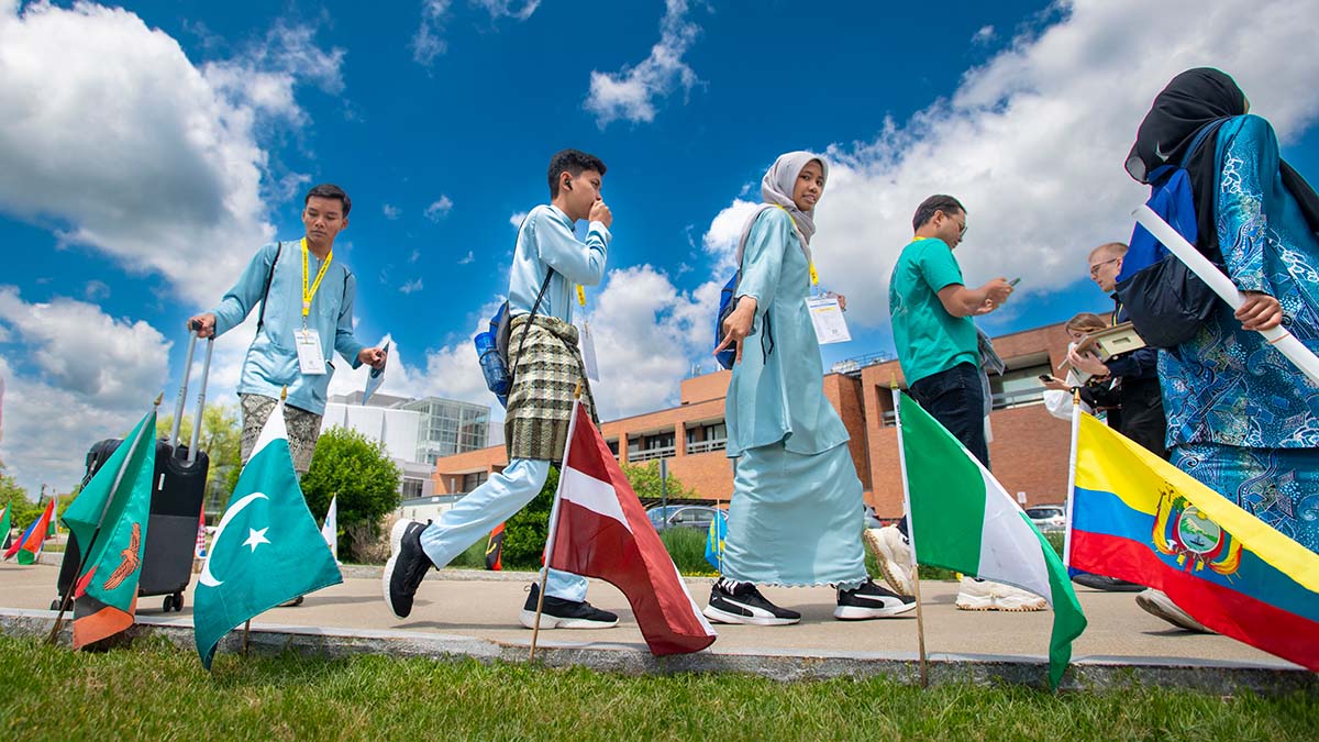 A group of international students walking on campus with national flags displayed along the pathway.