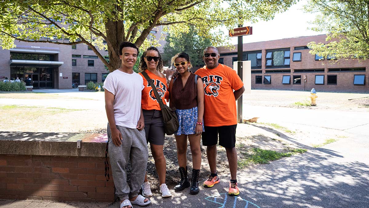 A family posing for a picture on campus, two members wearing matching R I T shirts.