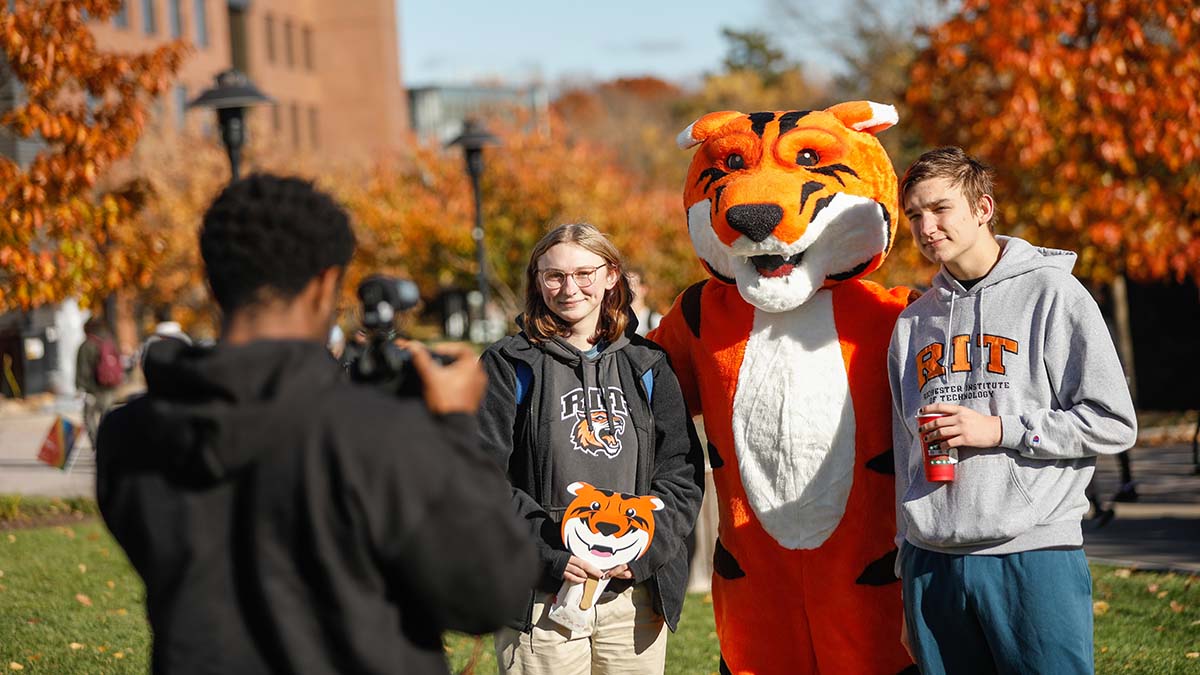 Students posing with the R I T tiger mascot while someone takes their photo.