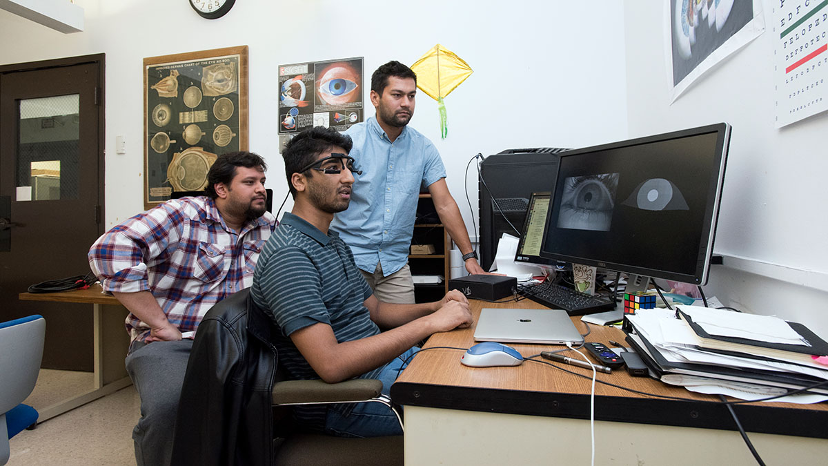 Three people reviewing eye-tracking software on a computer in a research lab.