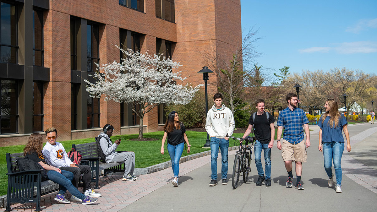 Students walking and chatting on the R I T campus path during a spring day.