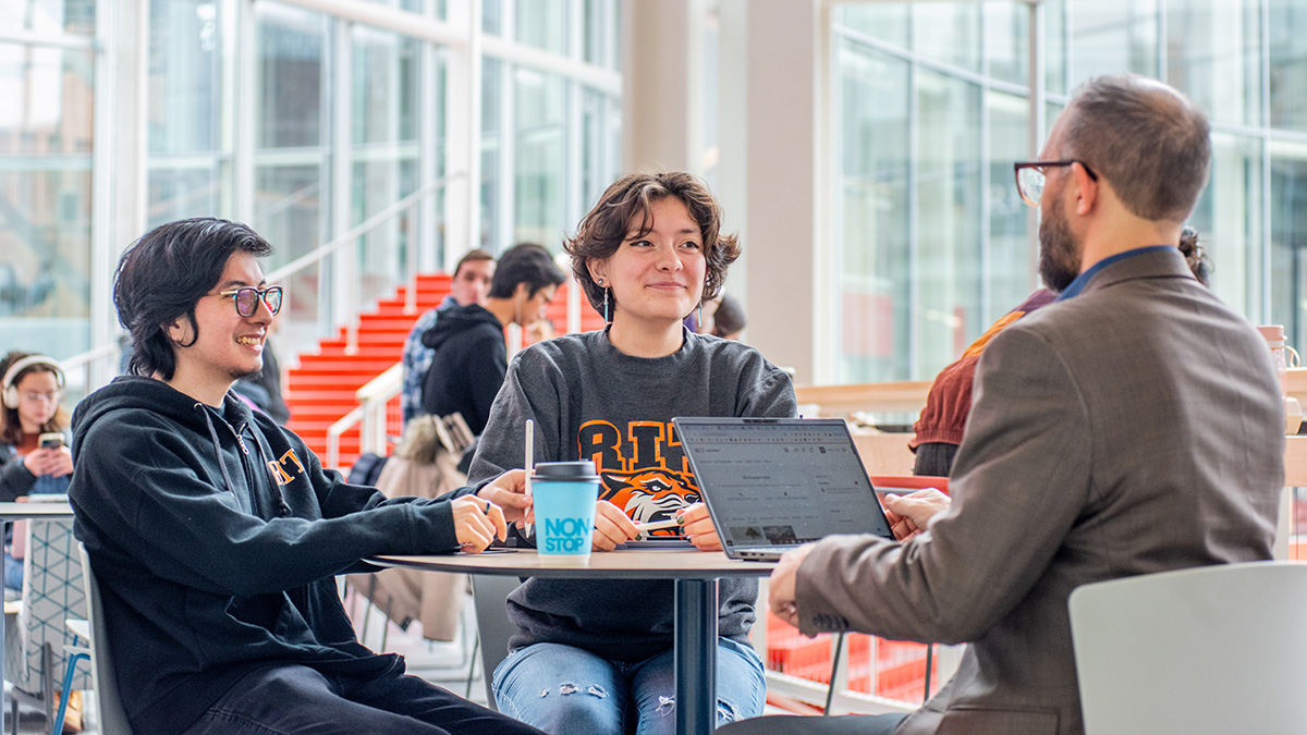 Two students talking to an employee in a bright indoor space