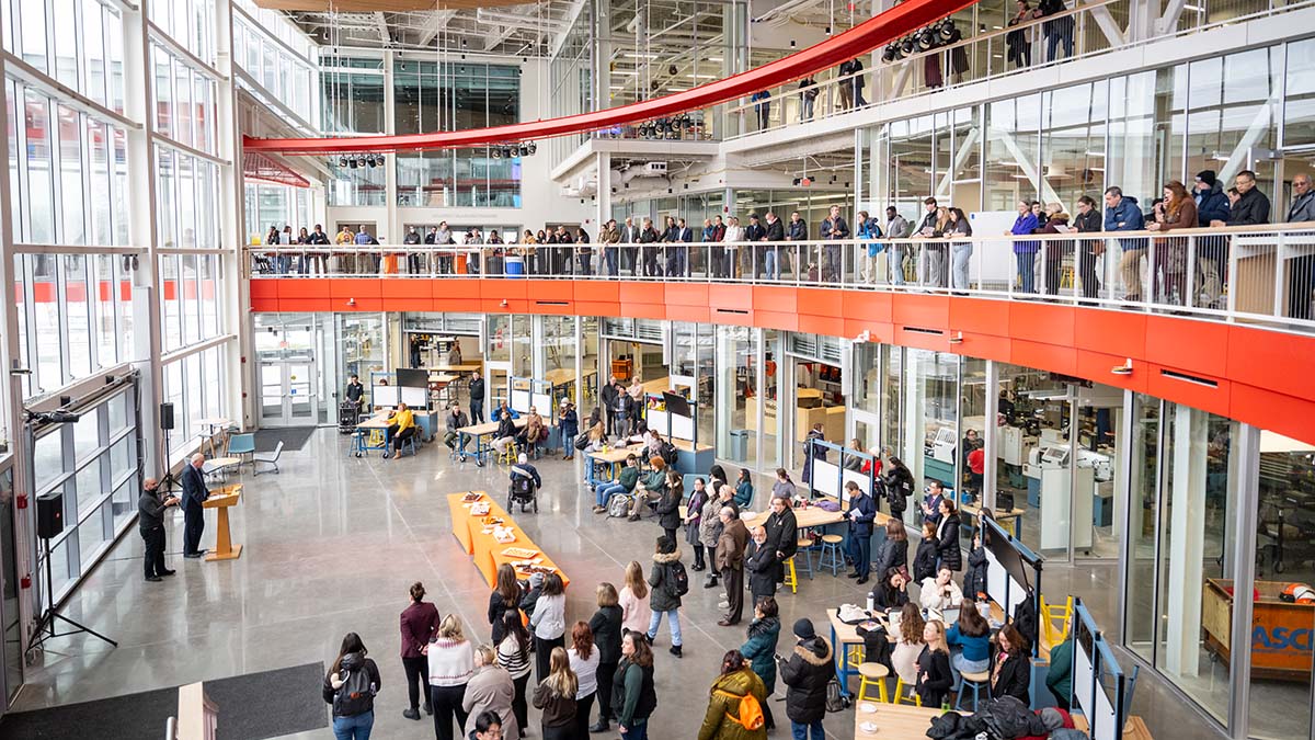 A large, bright indoor space with people gathering on two levels around tables and presentations.