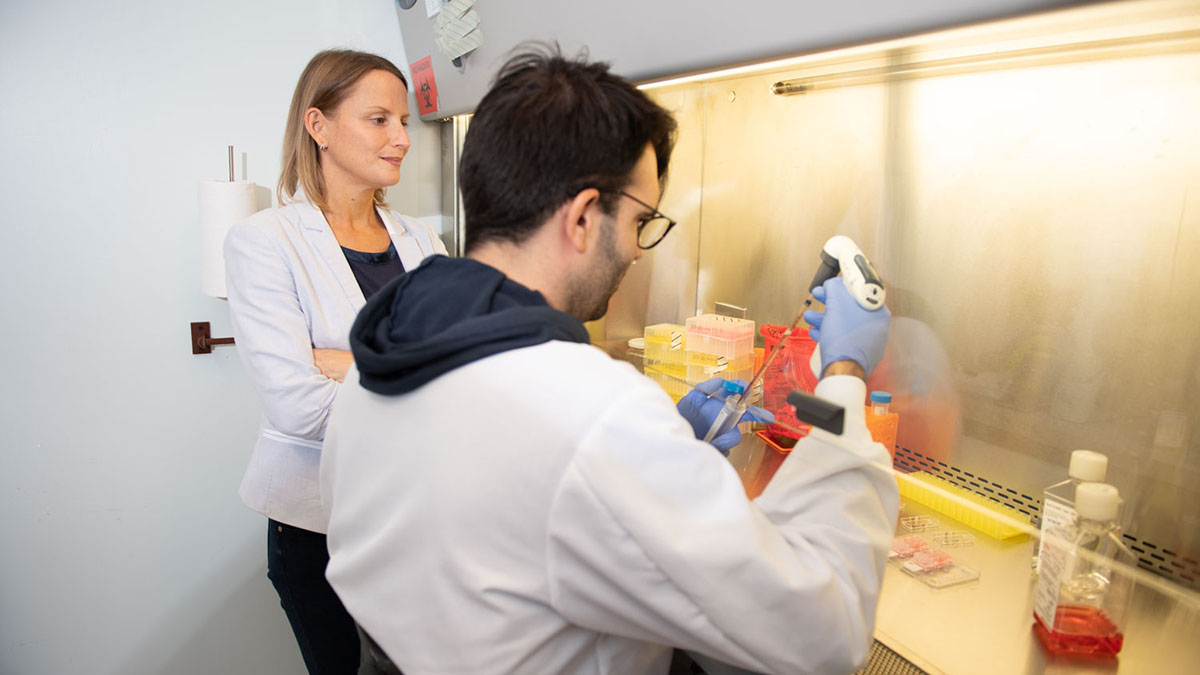 A researcher in a white coat working with a faculty member in a lab.