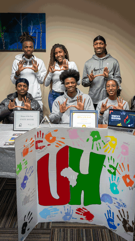 a group of students stand in front of a sign reading "UH" with handprints