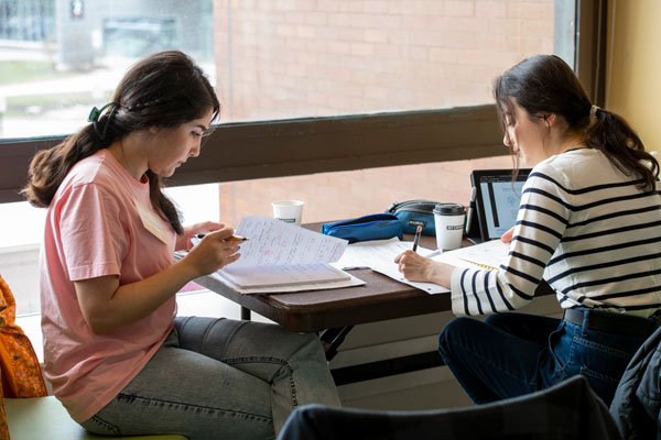 two students sit at a table doing work together