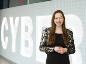An R I T student standing in front of a wall that says Cyber on it.