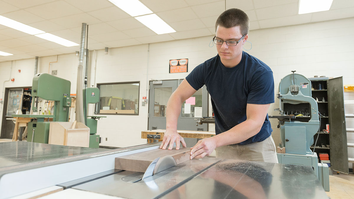 A man cutting wood with a table saw in a woodworking workshop.