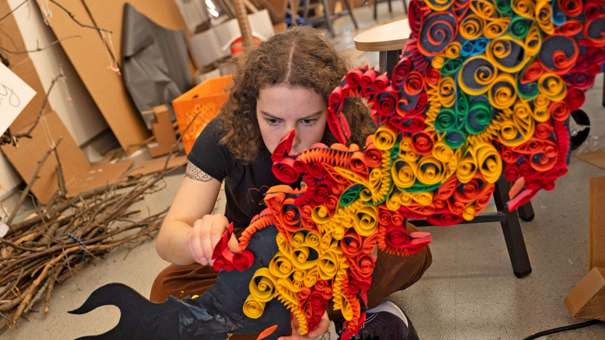 A student works on a colorful papercraft construction.