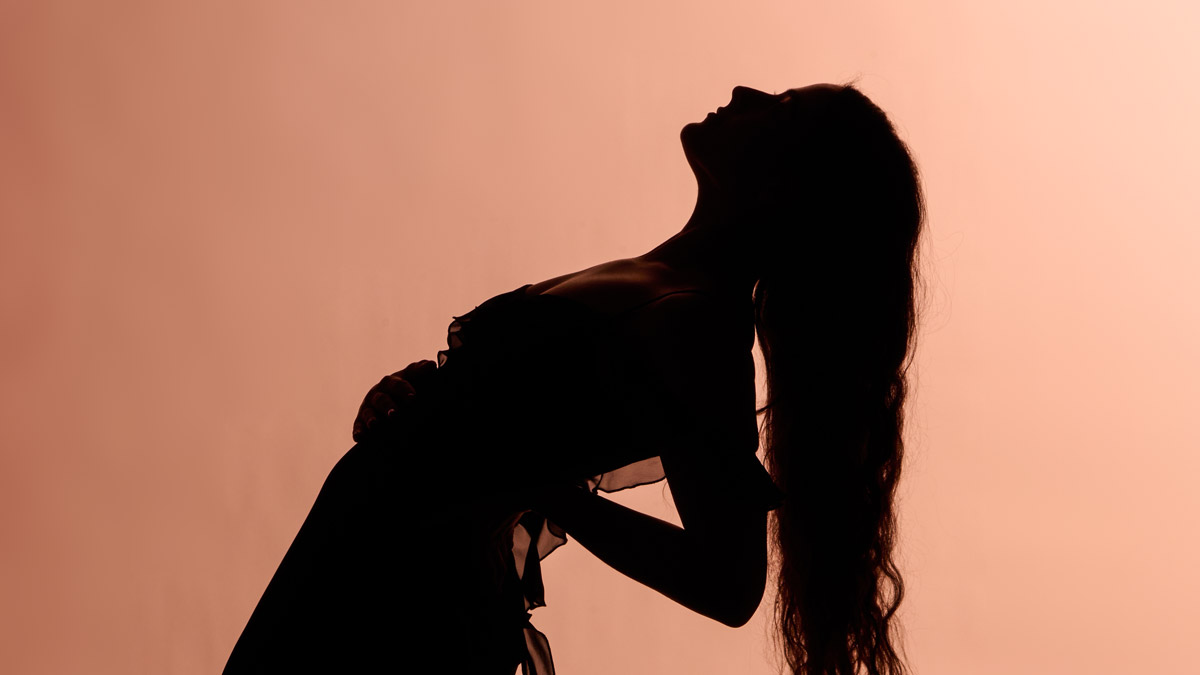 A silhouetted figure with long hair bends backwards in profile in front of a peach-colored backdrop.