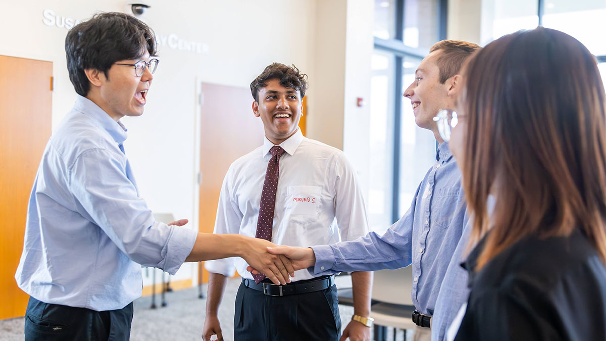 Students shaking hands and networking in a bright academic building.