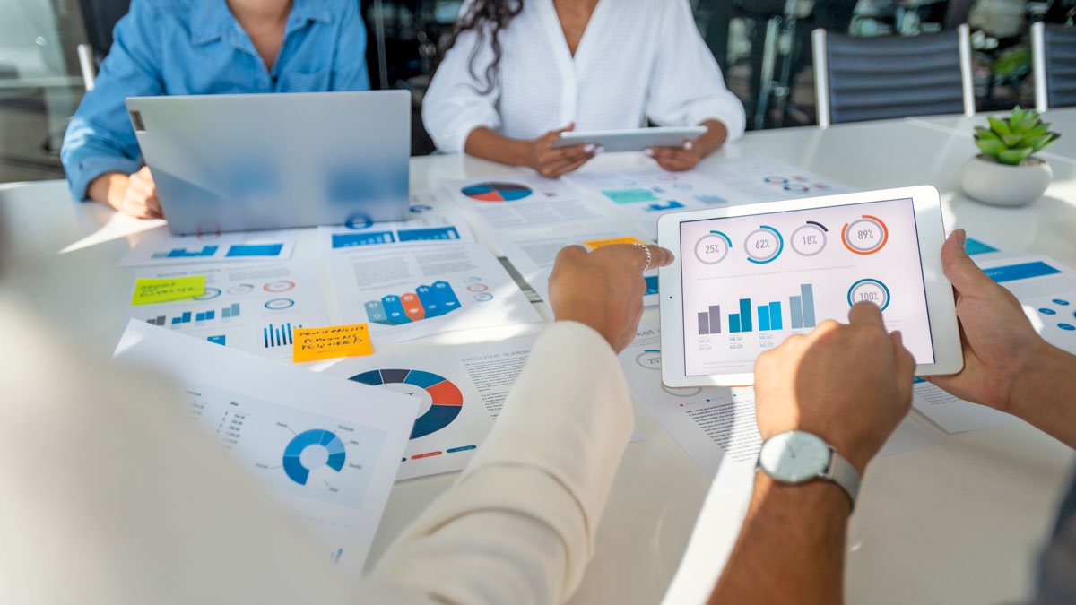 A table and tablet have infographics on them and two hands are point at the graphics.