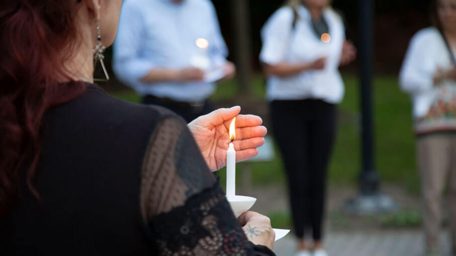 Individual in a black shirt is shown holding a candle at a candlelight vigil