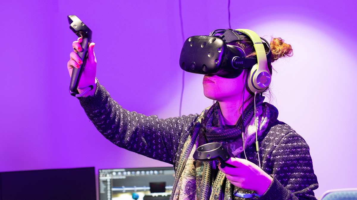 Student uses VR headset and motion controllers in a purple room.