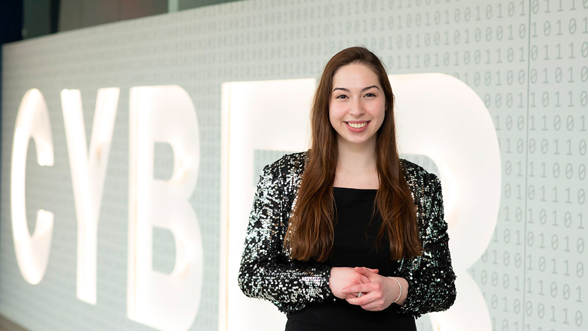 Student stands in front of a sign with the word CYBER written big with zeros and ones on the background.