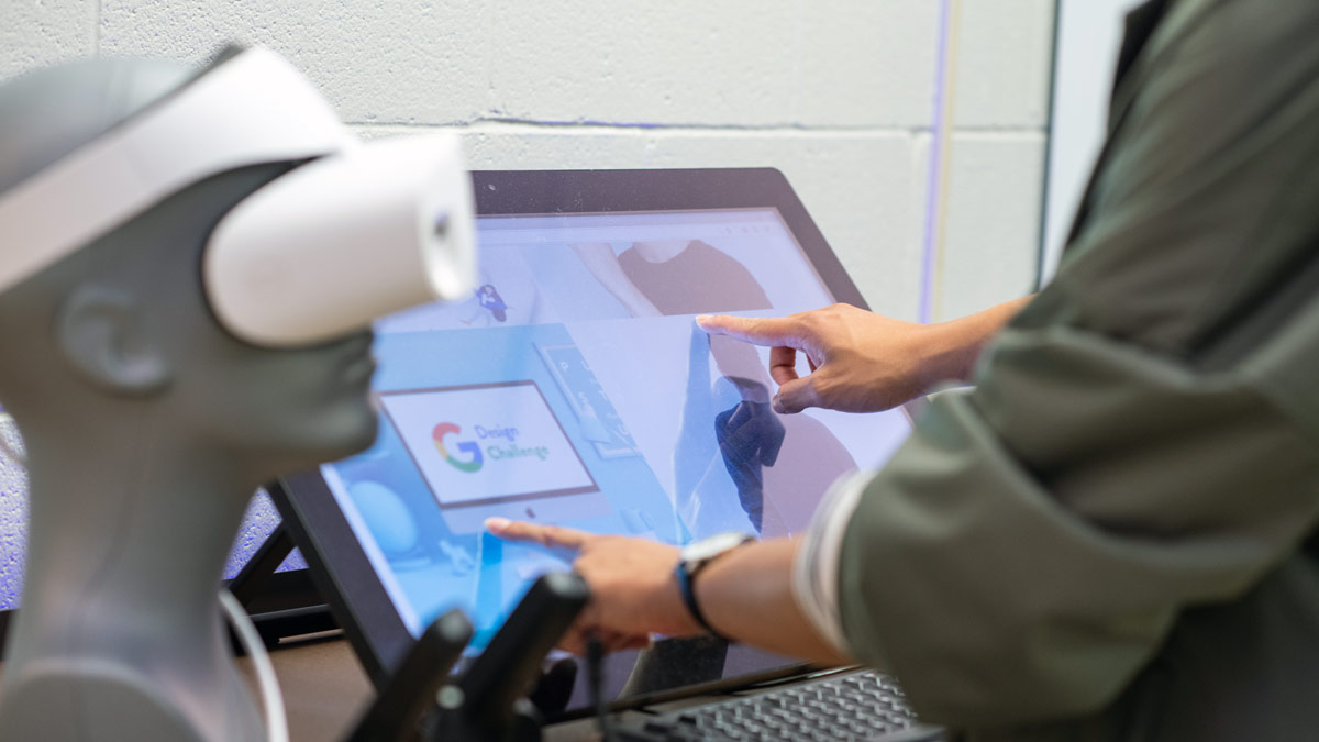 A student uses a touchscreen display. A VR headset is on a mannequin head in the foreground.