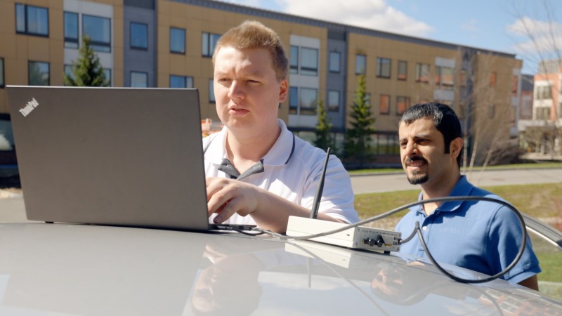 Geoff Twardokus, an electrical and computer engineering Ph.D. student, and Hanif Rahbari, assistant professor of cybersecurity, stands next to a grey care wth a laptop propped up on its hood.
